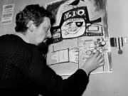 1957 London, England. Animation and Film. The office of a cartoon film unit. Cartoonist Bob Godfrey adds a watch to a poster on the wall of his studio.