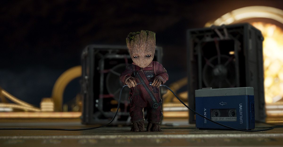 Baby Groot (voiced by Vin Diesel) prepares to rock out while his friends fight a giant Abelisk.