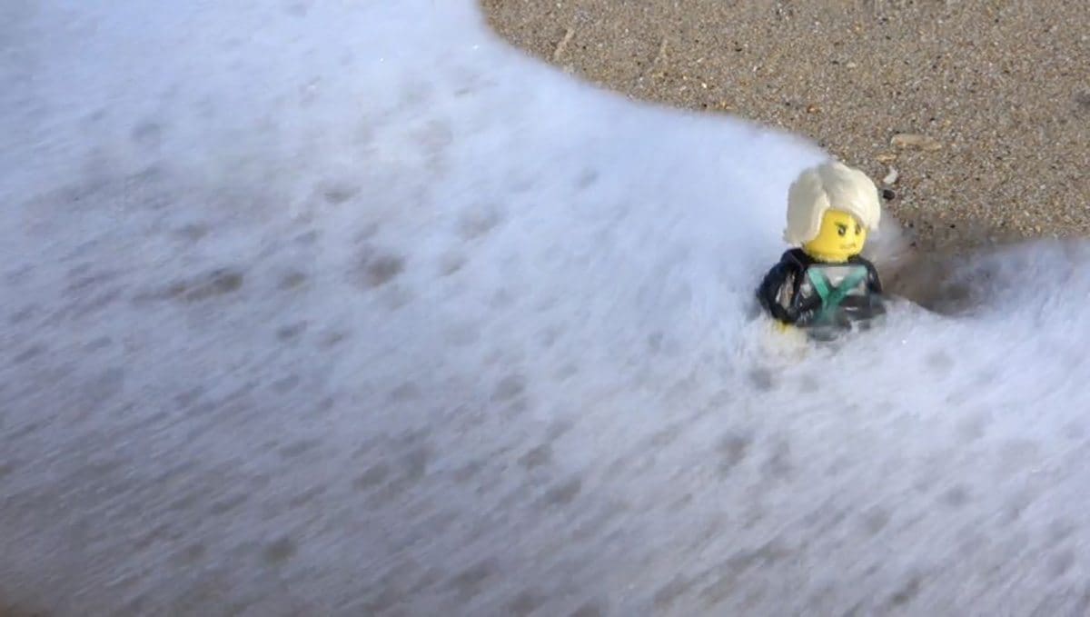 Closer view of the concept minifig amongst sand and foam at Bondi Beach.